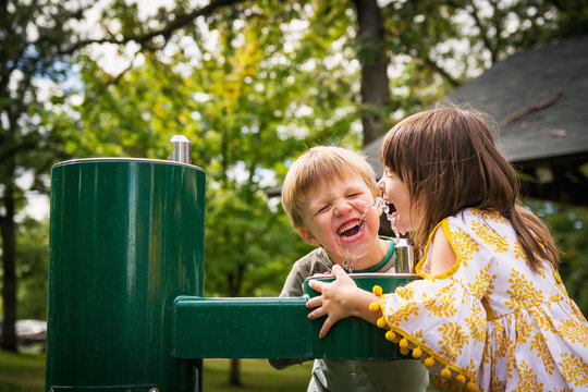 Two happy children drinking water from a water fountain