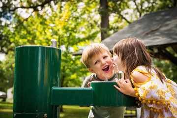 Two happy children drinking from a water fountain in a park in the summer, USA