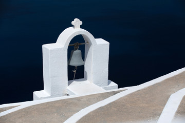 White bell tower of a Greek church on Santorini Island, Greece with sea in the background.