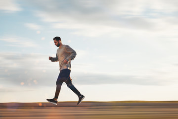 Young athlete in headphones and sports clothes and sneakers runs in the park. Lubricated background. Motion blur