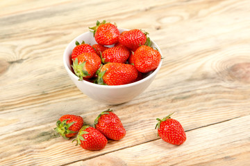 Ripe strawberry in a white bowl on a wooden background