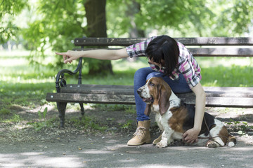 Woman sits on a bench in the park with his beautiful dog and shows him which way to look.