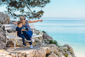 Mother and son sitting on the bench at the rocky beach