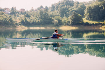 A Young single scull rowing competitor paddles on the tranquil lake © FS-Stock