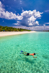 Young man snorkling in tropical lagoon with over water bungalows, Maldives