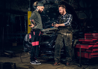 Obraz na płótnie Canvas Two bearded mechanics inspecting car's engine parts.