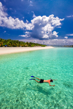 Young Man Snorkling In Tropical Lagoon With Over Water Bungalows, Maldives