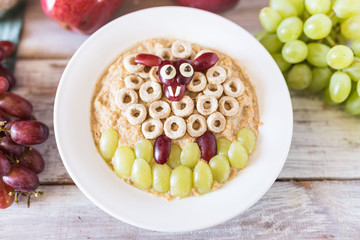 Homemade oatmeal porridge with a funny grape decoration on plate