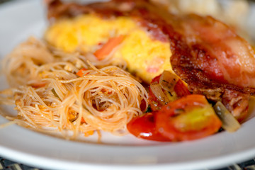 Asian dish - fried noodles with egg, tomato and bacon close-up on a plate