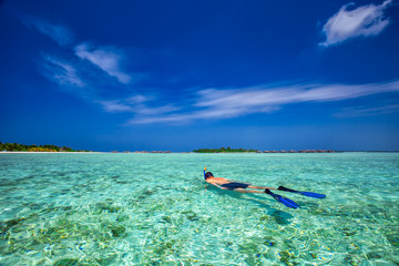 Young man snorkling in tropical lagoon with over water bungalows, Maldives - obrazy, fototapety, plakaty