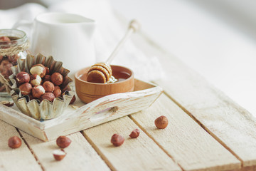 Honey in the wooden bowl, hazelnuts and jar with milk on the wooden tray