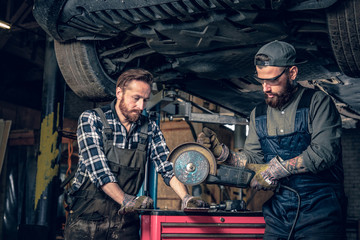Obraz na płótnie Canvas Two b mechanics working with an angle grinder in a garage.