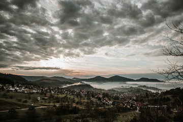 Fototapeta premium Village in the mountains with clouds and fog and sun in sunset