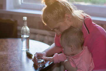 A young mother and a beautiful baby are sitting at the kitchen table on which stands a bottle of...
