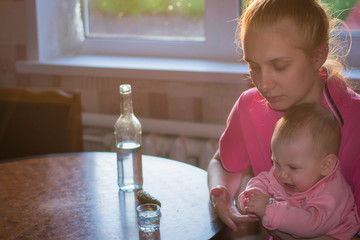 A young mother and a beautiful baby are sitting at the kitchen table on which stands a bottle of...