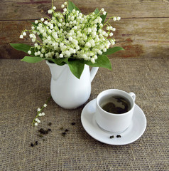 In a cup green tea is given. The bouquet of lilies of the valley is in a jug..