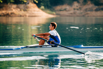 A Young single scull rowing competitor paddles on the tranquil lake - obrazy, fototapety, plakaty