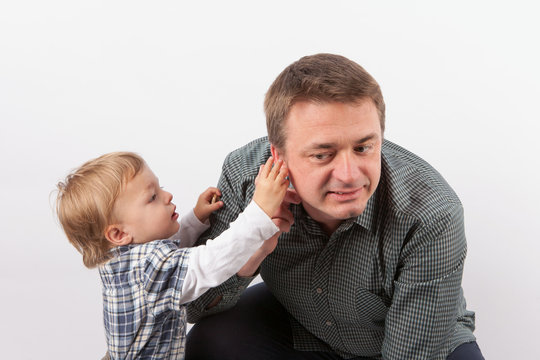 Toddler boy inspecting his father's hearing aid in his ear
