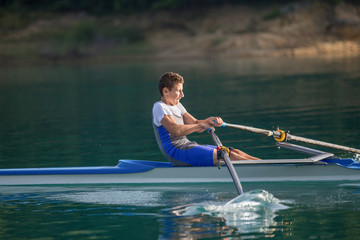 A Young single scull rowing competitor paddles on the tranquil lake