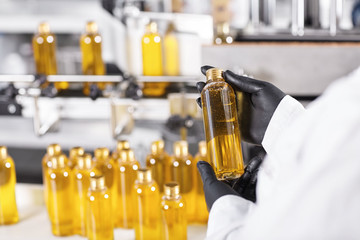Horizontal portrait of mass process at factory. Researcher standing near many bottles with yellow liquid holding one of them isolated over factory conveyor. Selective focus. Great success of factory