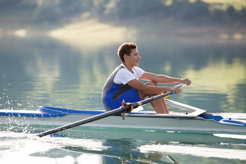 A Young single scull rowing competitor paddles on the tranquil lake