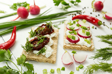 Vegetarian lunch of raw vegetables with ricotta cheese, sun dried tomatoes, herbs and radish on a white wooden table.