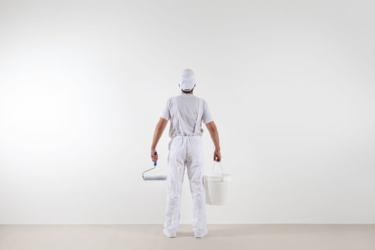 Rear view of painter man looking at blank wall, with paint roller and bucket, isolated on white room
