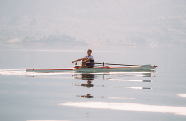 A Young single scull rowing competitor paddles on the tranquil lake