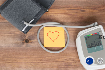 Healthy lifestyle concept, blood pressure monitor and a note with a heart shape on the brown wooden background.