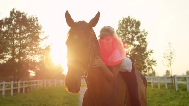 SLOW MOTION, CLOSE UP, DOF: Portrait of a beautiful blonde girl bareback riding and embracing her beloved mare at sunrise. Pretty woman horseback riding stunning horse on tranquil sunny summer morning