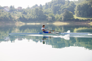 A Young single scull rowing competitor paddles on the tranquil lake