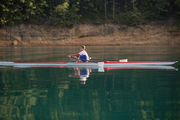 A Young single scull rowing competitor paddles on the tranquil lake