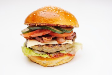 Appetizing burger with chop, bacon, bacon, cucumber, greens, salad on white background