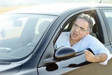 Road rage concept - irritated man screams and gestures while driving the car