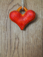 Red handmade heart hanging on cord on wooden background.