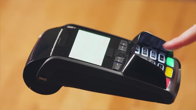 Close up shot of a woman's hands, who pays for a purchase with a bank card, she leans her to the terminal, then enters a pin code to withdraw funds