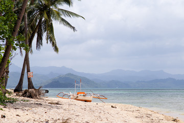 View of the boat on the beach with palm trees. In the background of the island.