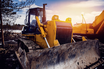Yellow bulldozer with caterpillars against the sky with a glare of the sun. Concept of road and...