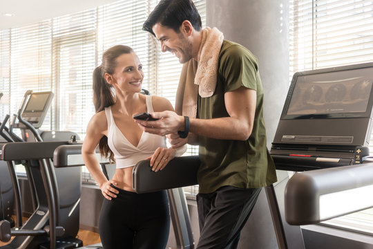 Young couple smiling while communicating on the mobile phone during break at the fitness club