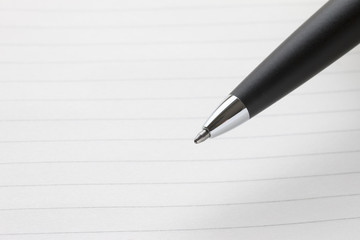 黒いボールペンのペン先、罫線入りのノートの背景