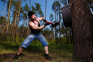 Strong healthy adult ripped man with big muscles hitting car tyre with big hammer