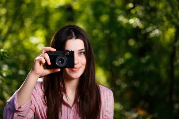 Young beautiful girl taking photos with retro film camera in the park