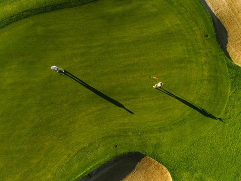 Aerial view of golfers playing on course - a golf course with a green and a white flag