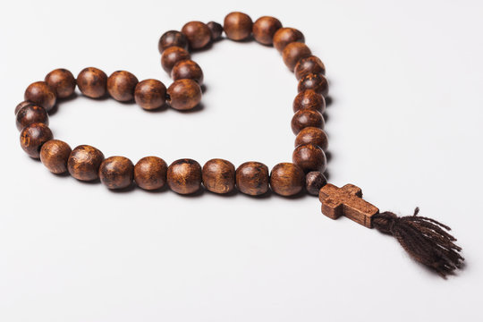 Rosary and a cross on a light gray background. in the shape of a heart