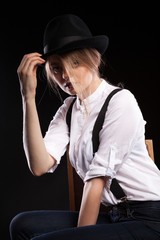 Gorgeous blonde woman with suspenders and white shirt wearing a hat on black background in studio photo
