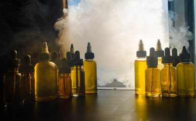 Vape concept. Smoke clouds and vape liquid bottles on window with sunlight on background. Light...