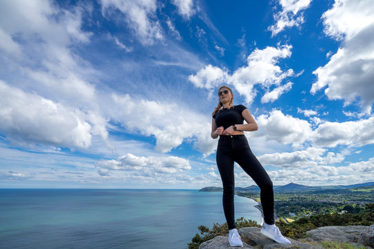 young beautiful girl female model photographer posing on top of the hill people embracing nature with open arms sea clouds blue sky tripod camera backpack sport clothes