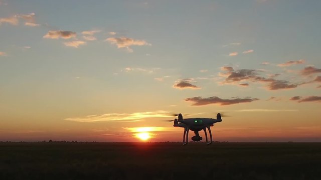 A drone with camera over a field flies at sunset. The operator moves after him. View from the eyes.