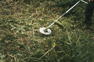 Gasoline trimmer head on green grass. Round trimmer blade.