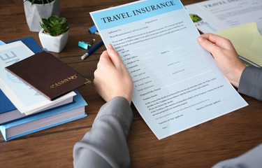 Fototapeta premium Woman sitting at workplace and holding blank travel insurance form, closeup